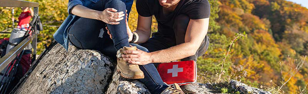 Mann mit Verbandtasche kümmert sich um verletzte Frau in den Berge