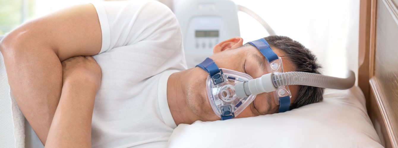 Ein Mann liegt im Bett und trägt eine CPAP-Maske zur Therapie von Schlafapnoe