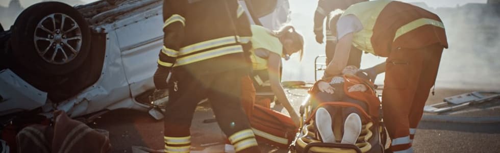 Feuerwehrmänner legen eine verletzte Person an einem Unfallort von einem Rettungstuch auf eine Rettungstrage