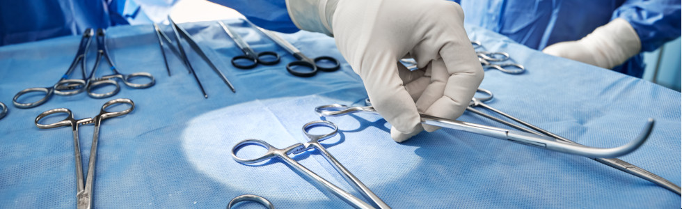 Chirurg greift nach medizinischer Zange auf Ablage mit anderen Instrumenten im OP-Saal