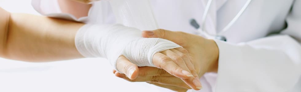 Arzt verbindet Hand mit Kompresse und Fixierbinde