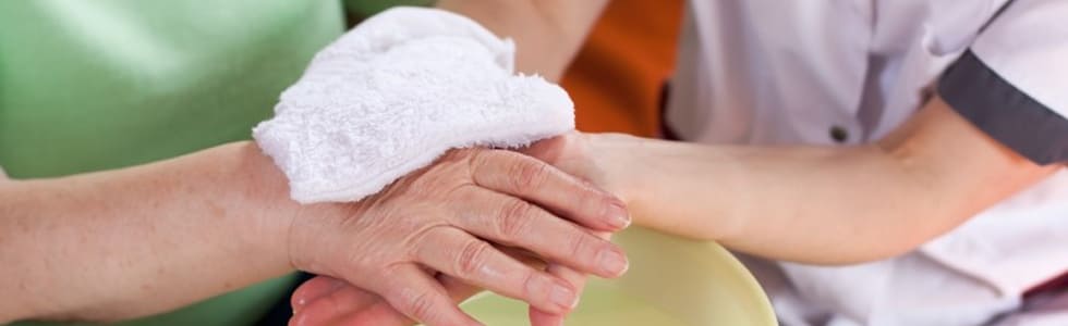 Eine Frau säubert die Hand einer Seniorin mit Einmal-Waschhandschuhen