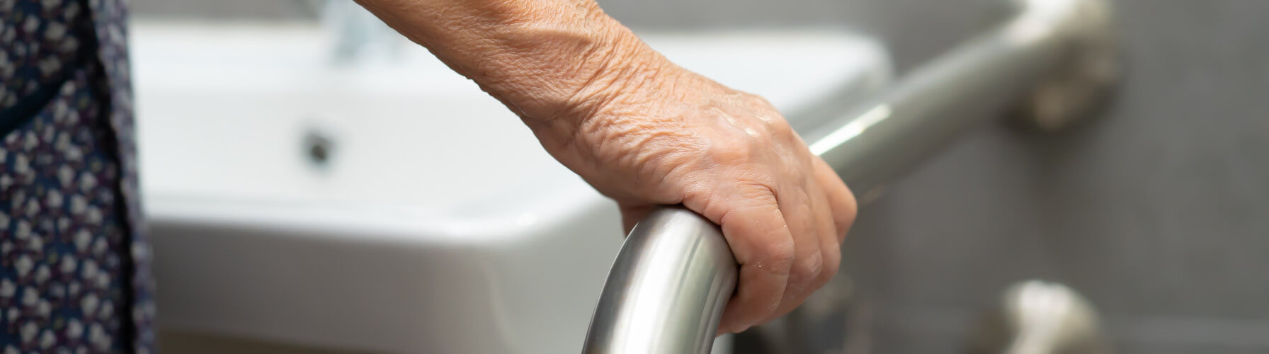 Eine Frau hält sich an einem Haltegriff fest – ihr Bad ist mit WC Hilfsmitteln ausgestattet 
