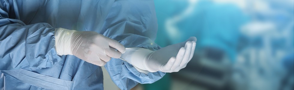 Ein Arzt zieht einen OP Handschuh an – medizinische Schutzkleidung ist im OP Pflicht