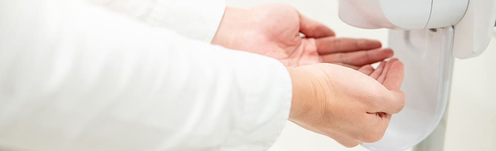 Ein Arzt desinfiziert sich die Hände an einem Desinfektionsmittelspender