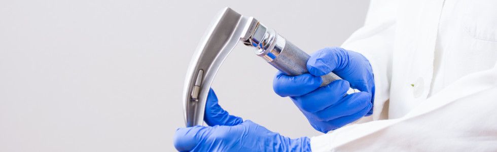 Arzt fasst an den Spatel des Laryngoskops mit blauen Handschuhen — jetzt Laryngoskop kaufen!