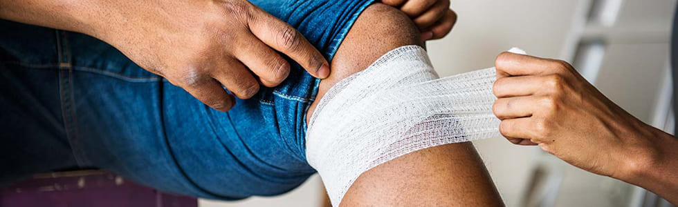 Frau verbindet das Knie eines Mannes mit Bandage aus einem Verbandkasten Nachfüllset