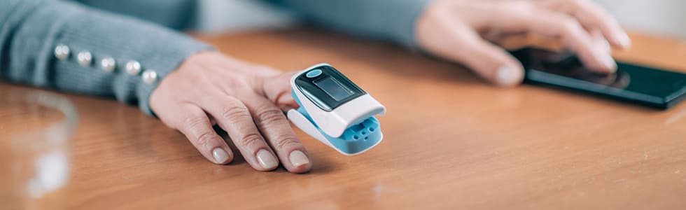 Die Hand einer Seniorin ist mit einem Fingerpulsoximeter versehen