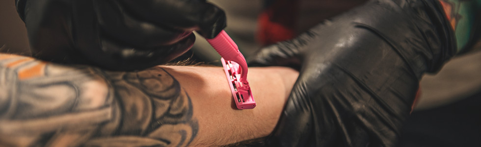 Ein Mann bereitet die Haut mit einem medizinischen Einwegrasierer auf ein Tattoo vor