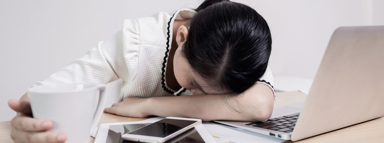 Eine Frau, die unter Tagesmüdigkeit leidet, sitzt schlafend am Schreibtisch