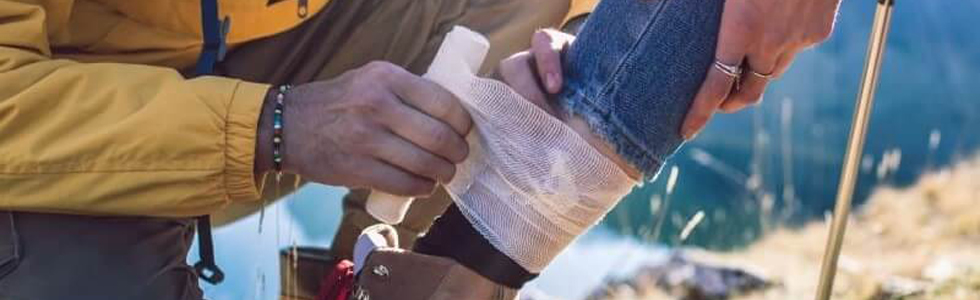 Ein Mann verbindet einer Frau den Knöchel mit einem Verband aus einer Erste Hilfe Tasche