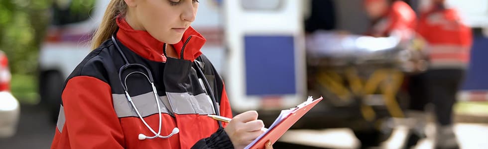 Notfallsanitäterin notiert vor Ambulanz mit Stift auf Klemmbrett Informationen – Organisationsmittel erleichtern solche Vorgänge
