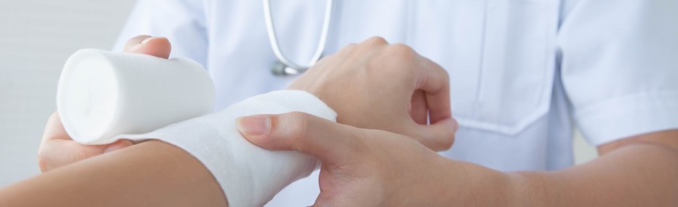 Ein Arzt verbindet die Hand eines Patienten mit Verbandstoffen aus dem Praxisbedarf