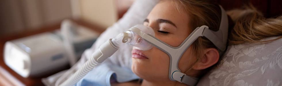 Frau schläft mit Maske, die mit CPAP-Zubehör ausgestattet ist