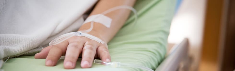 Eine Hand eines Mannes im Krankenhausbett ist mit Infusionszubehör ausgestattet